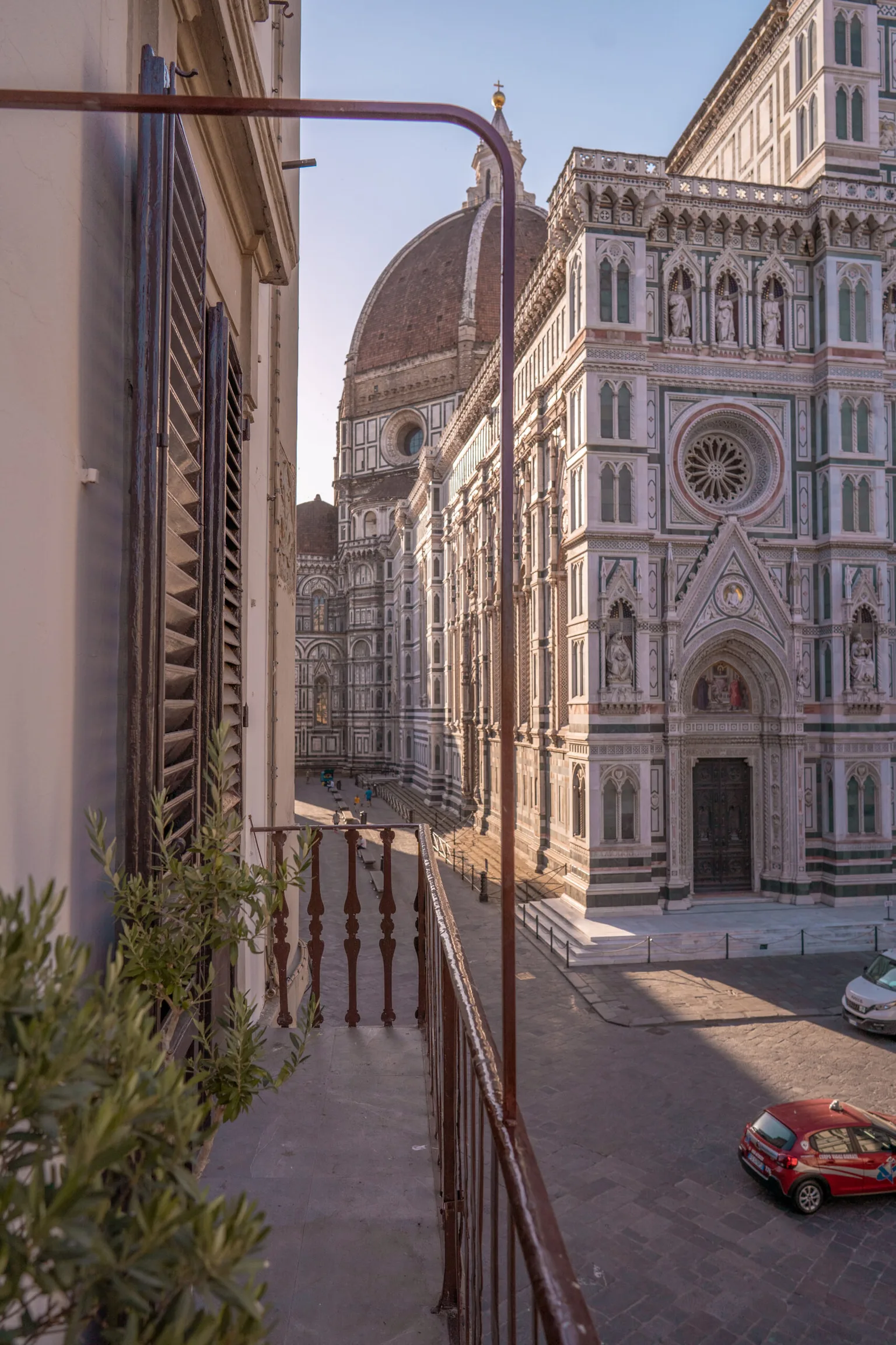 Balcony view overlooking the ornate marble façade and giant red-tiled dome of Florence's Cathedral of Santa Maria del Fiore at sunrise.
