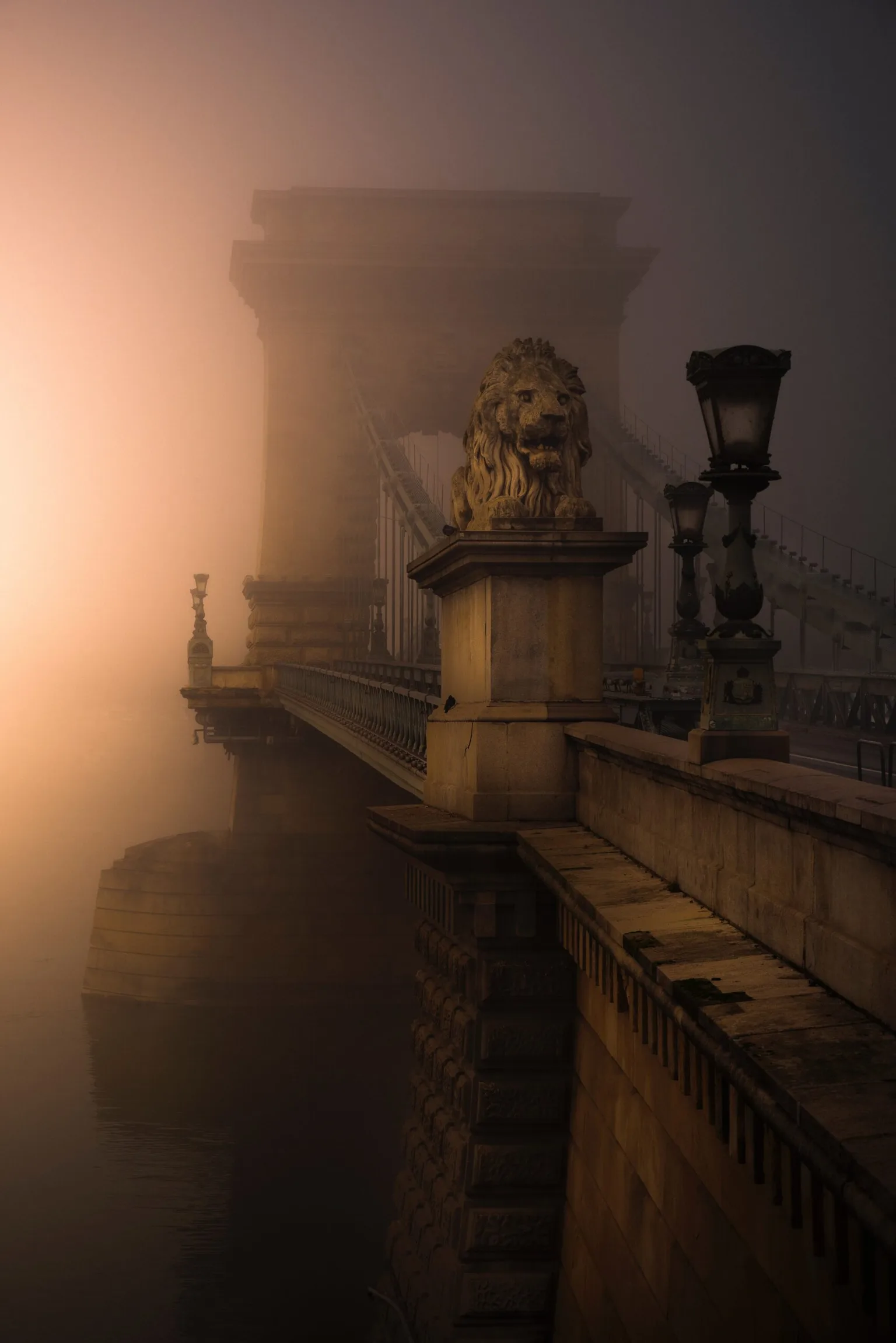 Fog-shrouded stone bridge at dawn with a lion statue and vintage lampposts fading into the mist