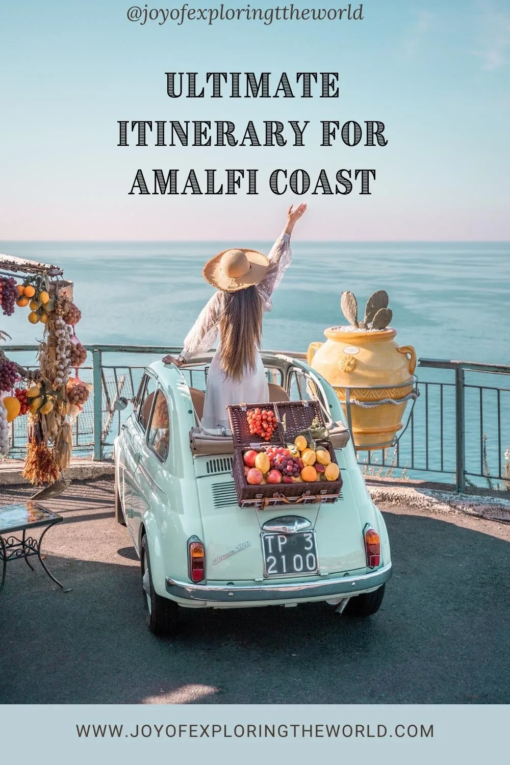 Woman in a sunhat standing in a vintage mint Fiat by the Amalfi Coast, overlooking the sea with a picnic basket of fruit.