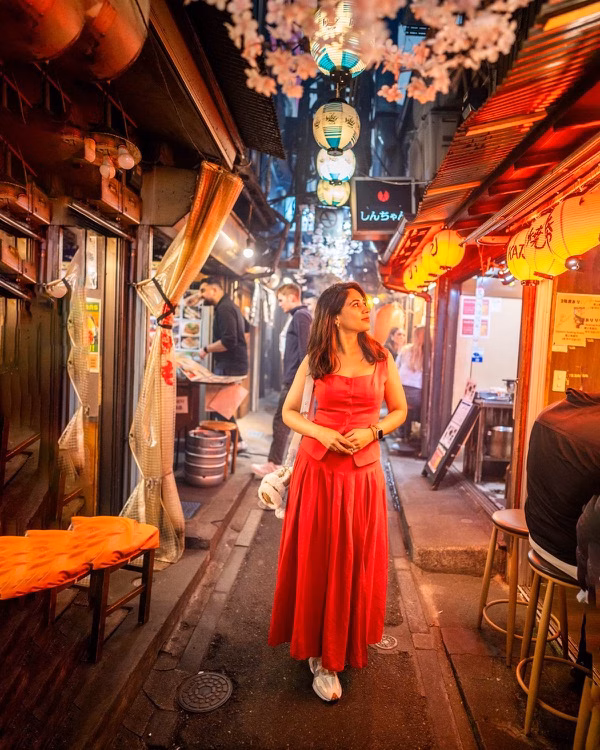 Woman in a red dress standing in a narrow lantern-lit alley lined with small bars and restaurants