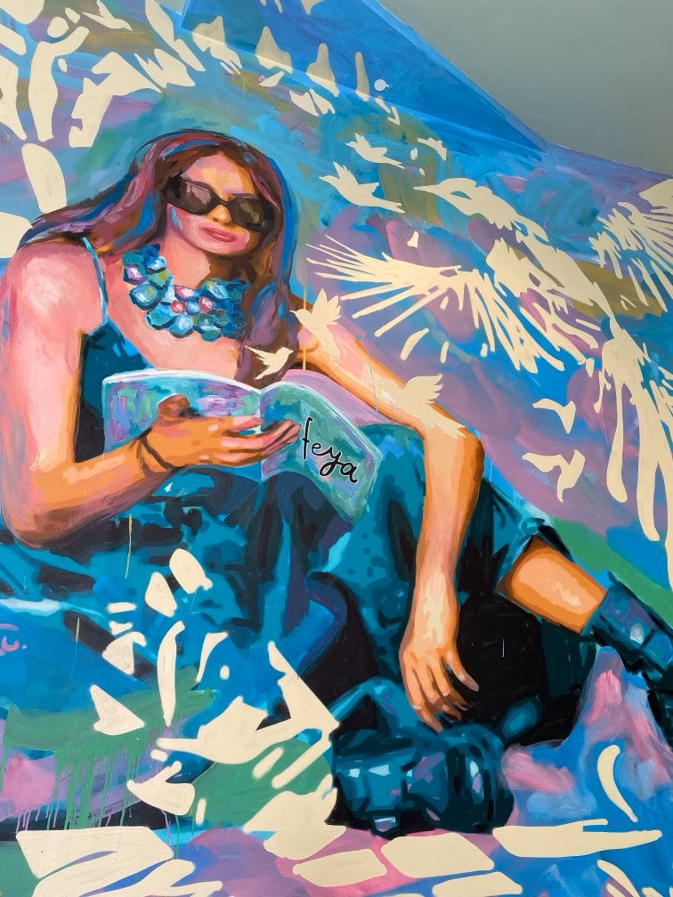 A colourful mural of a woman in sunglasses reading a book amid abstract blue and pink waves