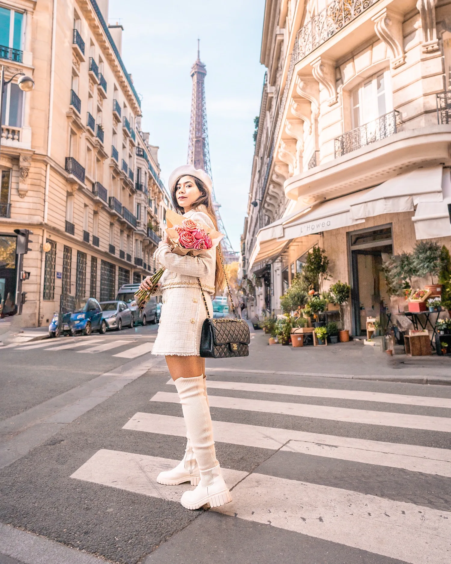 Young woman in a cream beret and matching tweed outfit holding a bouquet on a Parisian street with the Eiffel Tower in the background