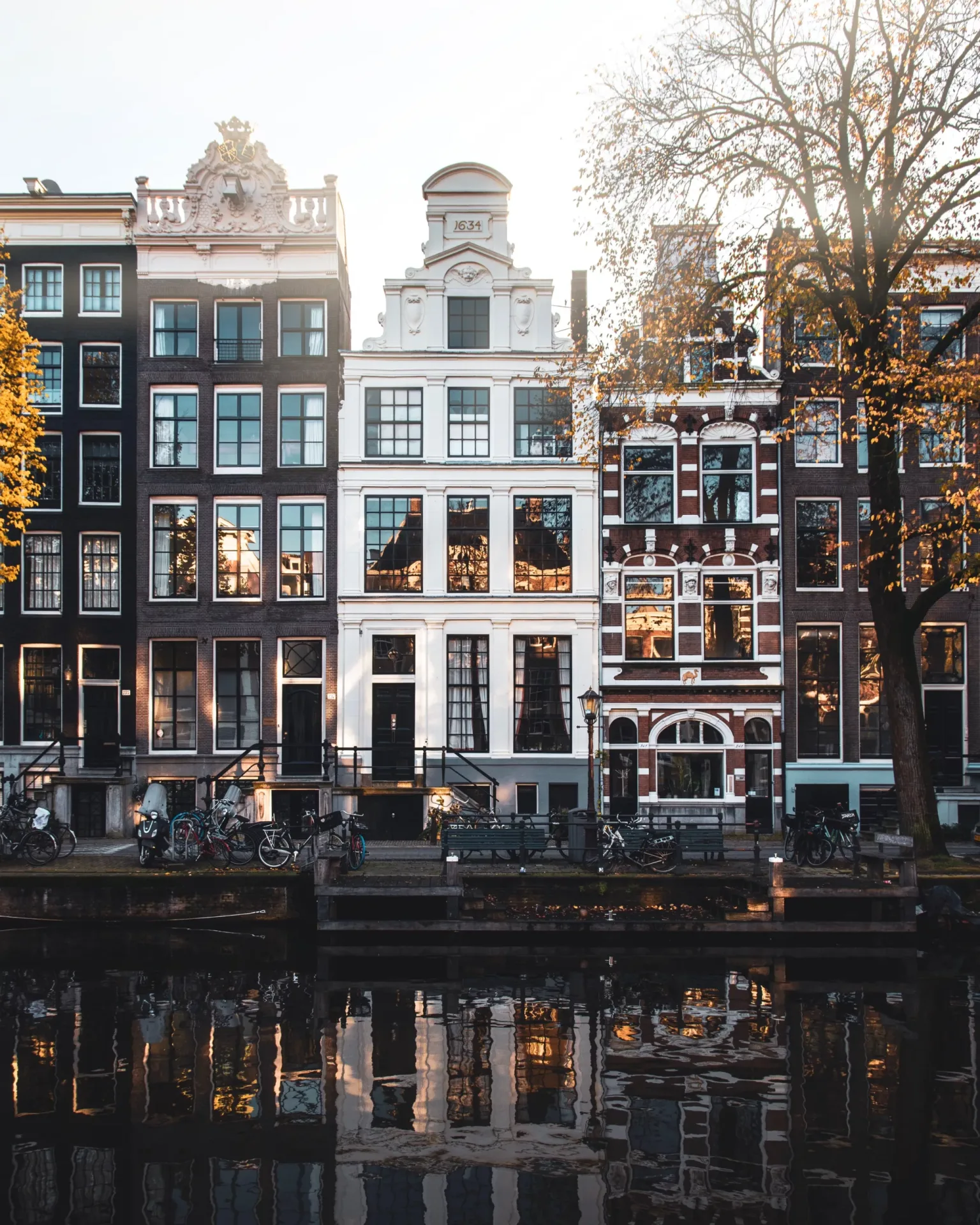 Tall narrow canal houses with ornate gables and bicycles lining the quay, their windows reflecting in the water at sunset.