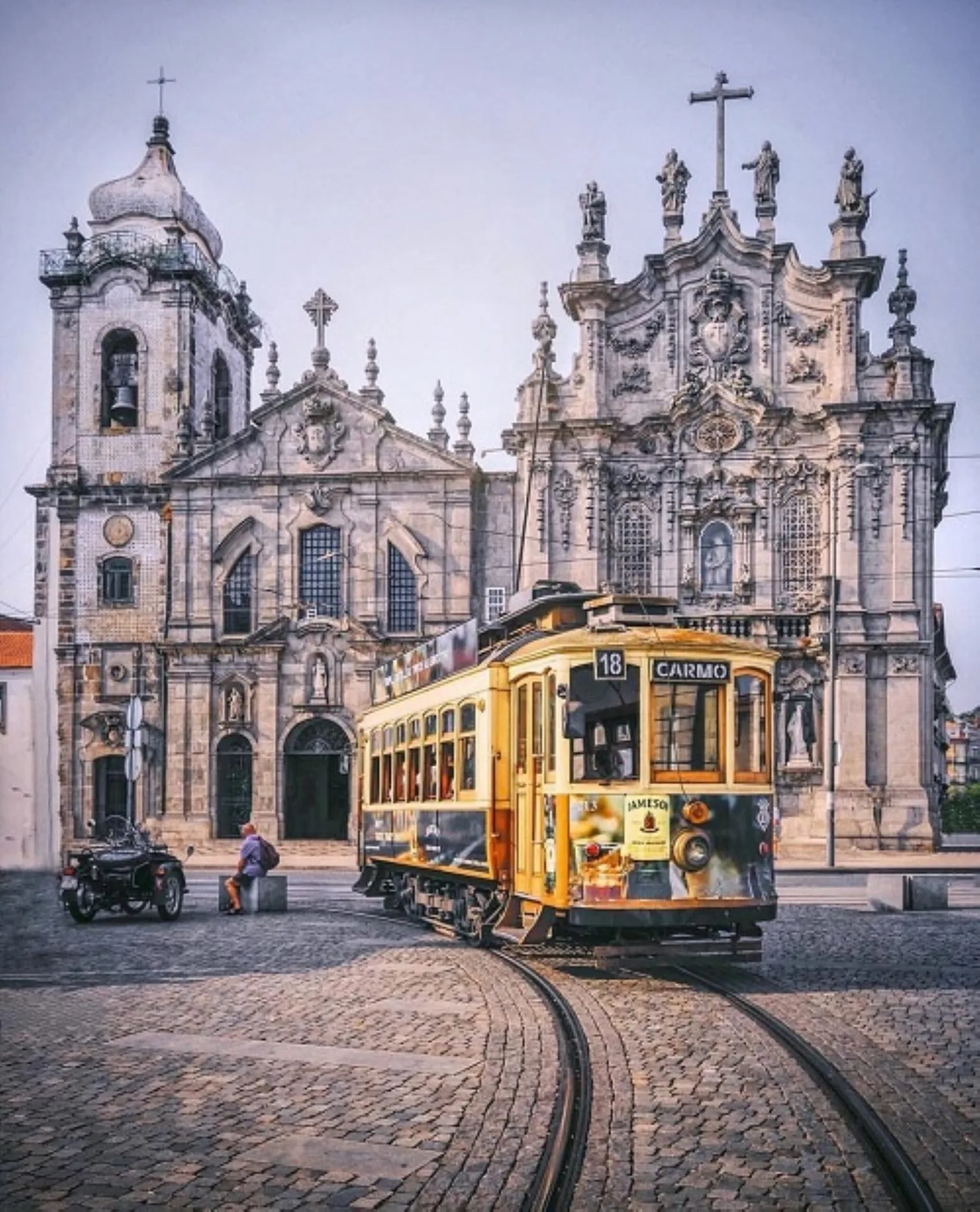 Yellow vintage tram turning on cobbled tracks in front of ornate baroque church façade in a European city square.