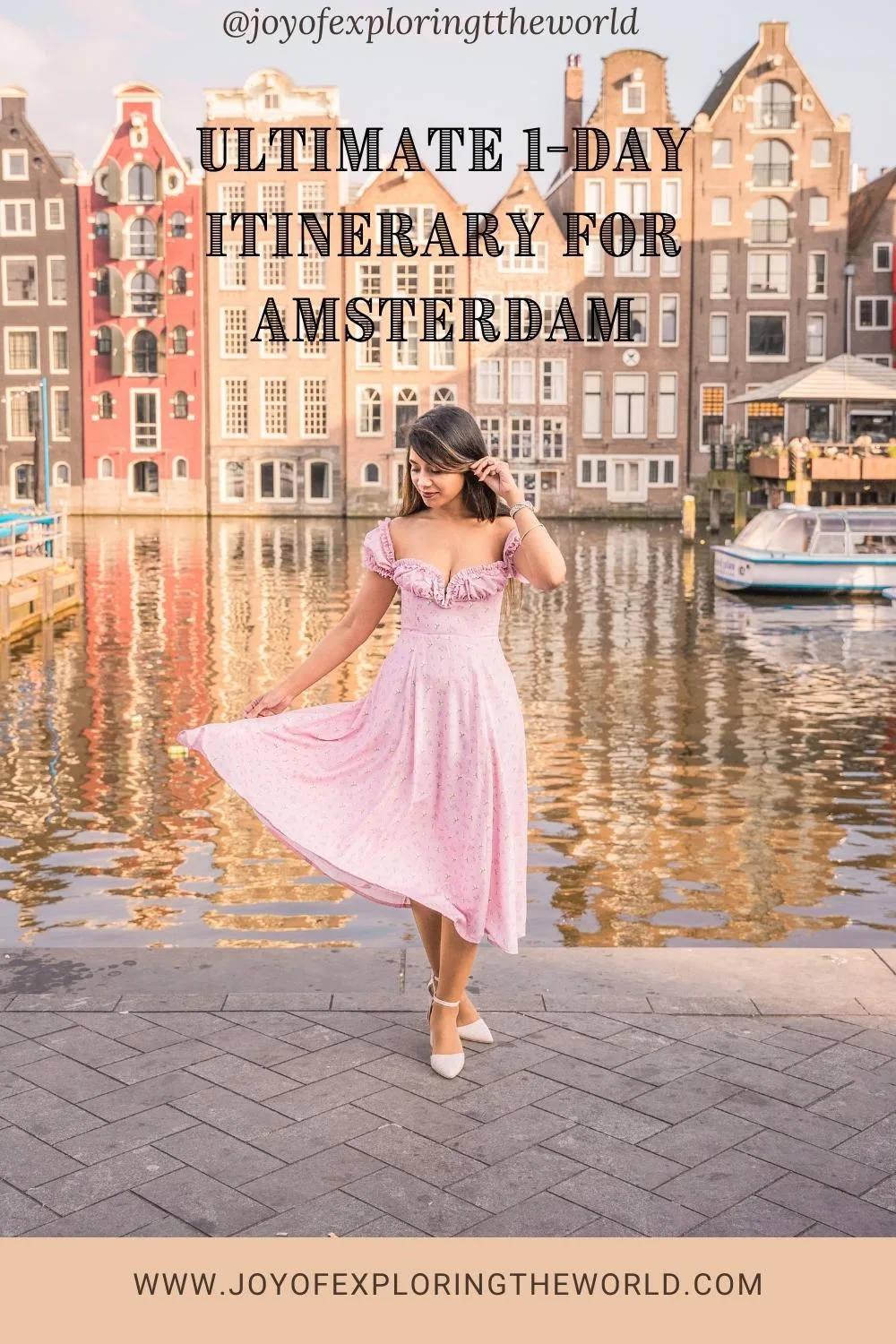 Woman in a pink dress posing by a canal with tall Amsterdam canal houses reflected in the water behind her.