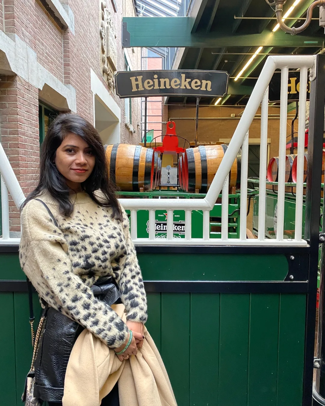 Woman standing inside the Heineken museum in front of wooden beer barrels and a green display.