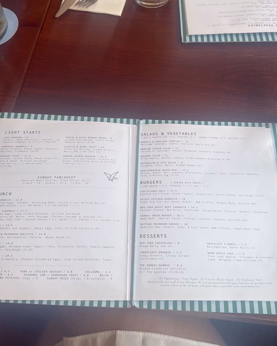 Open restaurant menu on a wooden table, showing brunch, salads, burgers and desserts