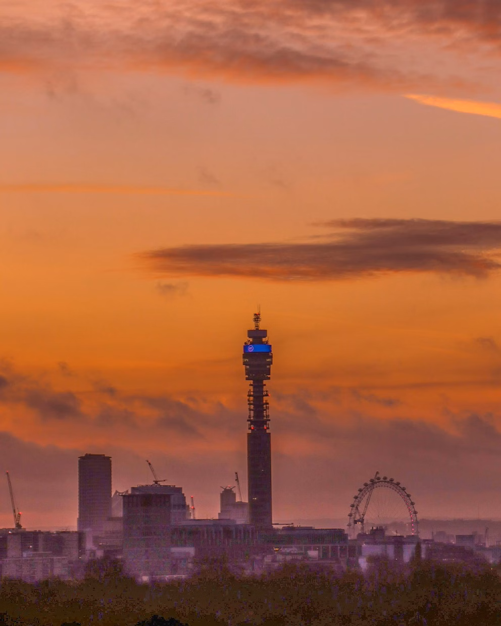 Sunset skyline with the London Eye and a tall tower silhouetted against an orange sky