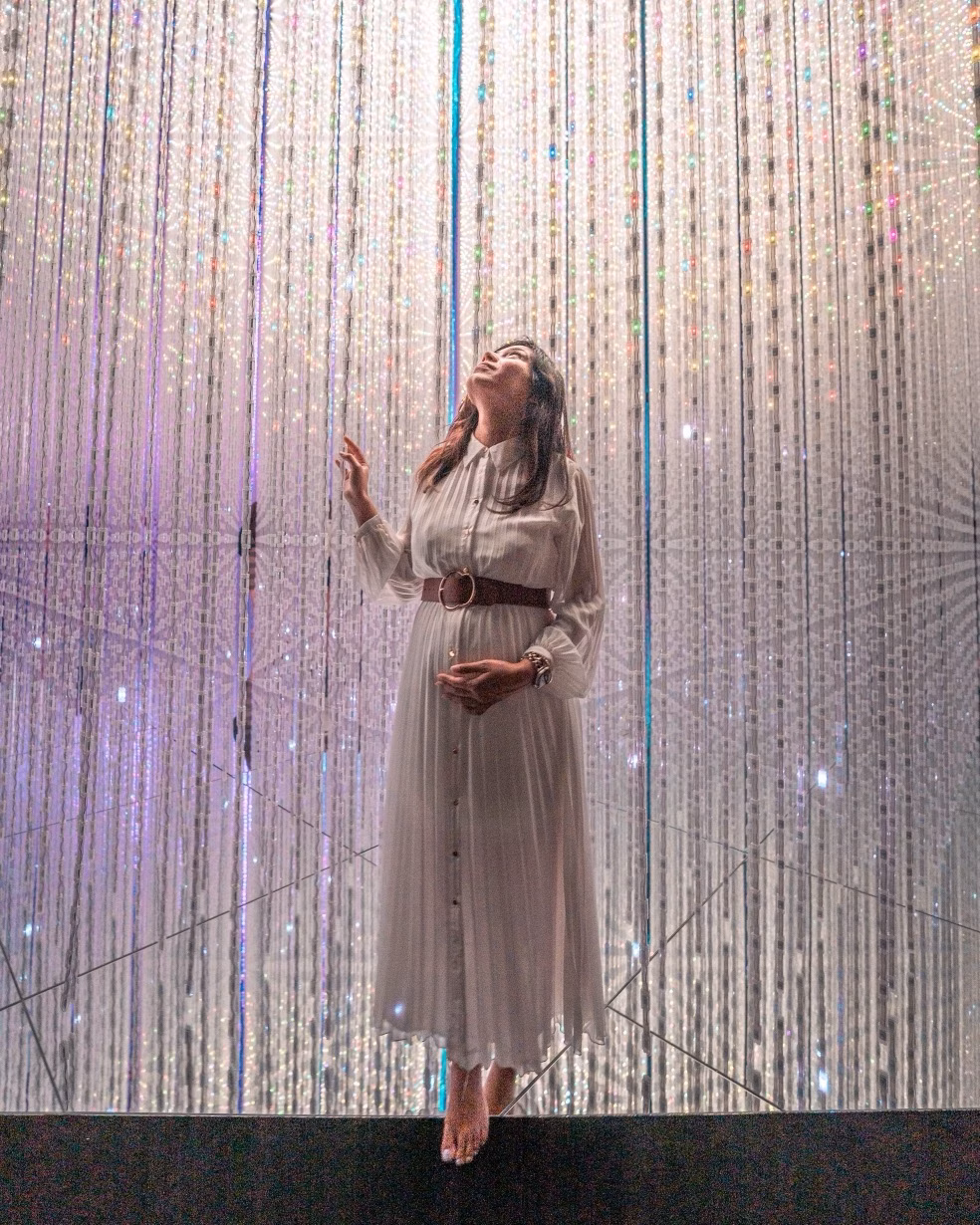 Woman in a white dress standing beneath a sparkling curtain of lights
