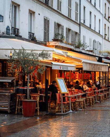 Outdoor café with red chairs and warm lights along a wet cobblestone street in a European city