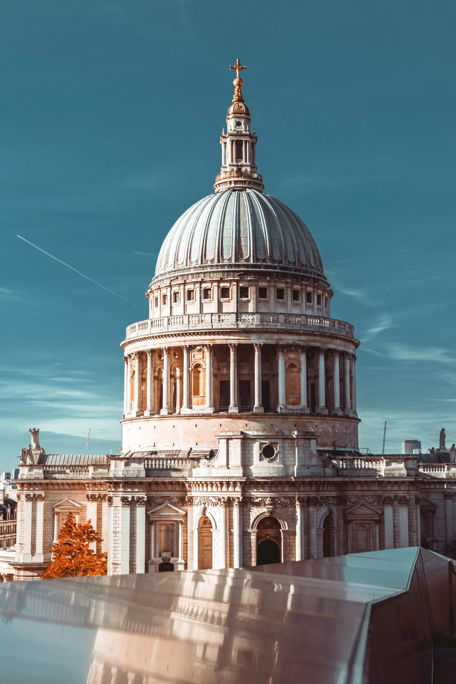 St Paul’s Cathedral dome rising against a clear blue sky, with ornate stone columns and a reflective foreground.