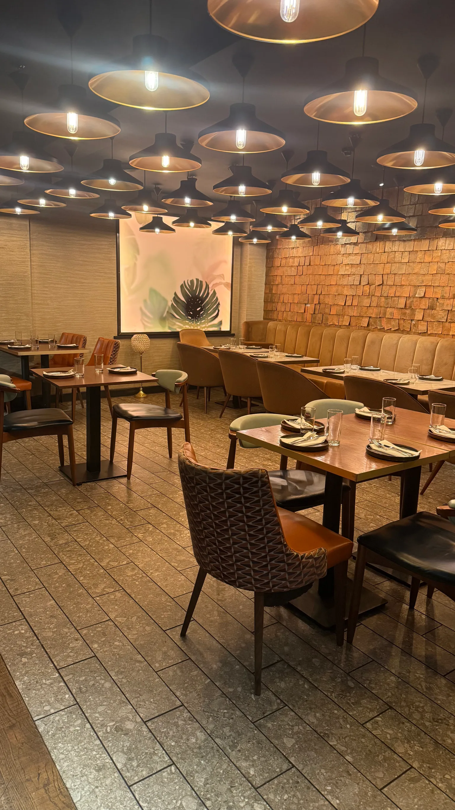 Cozy, modern restaurant interior with warm pendant lights, mixed seating and neatly set wooden tables.