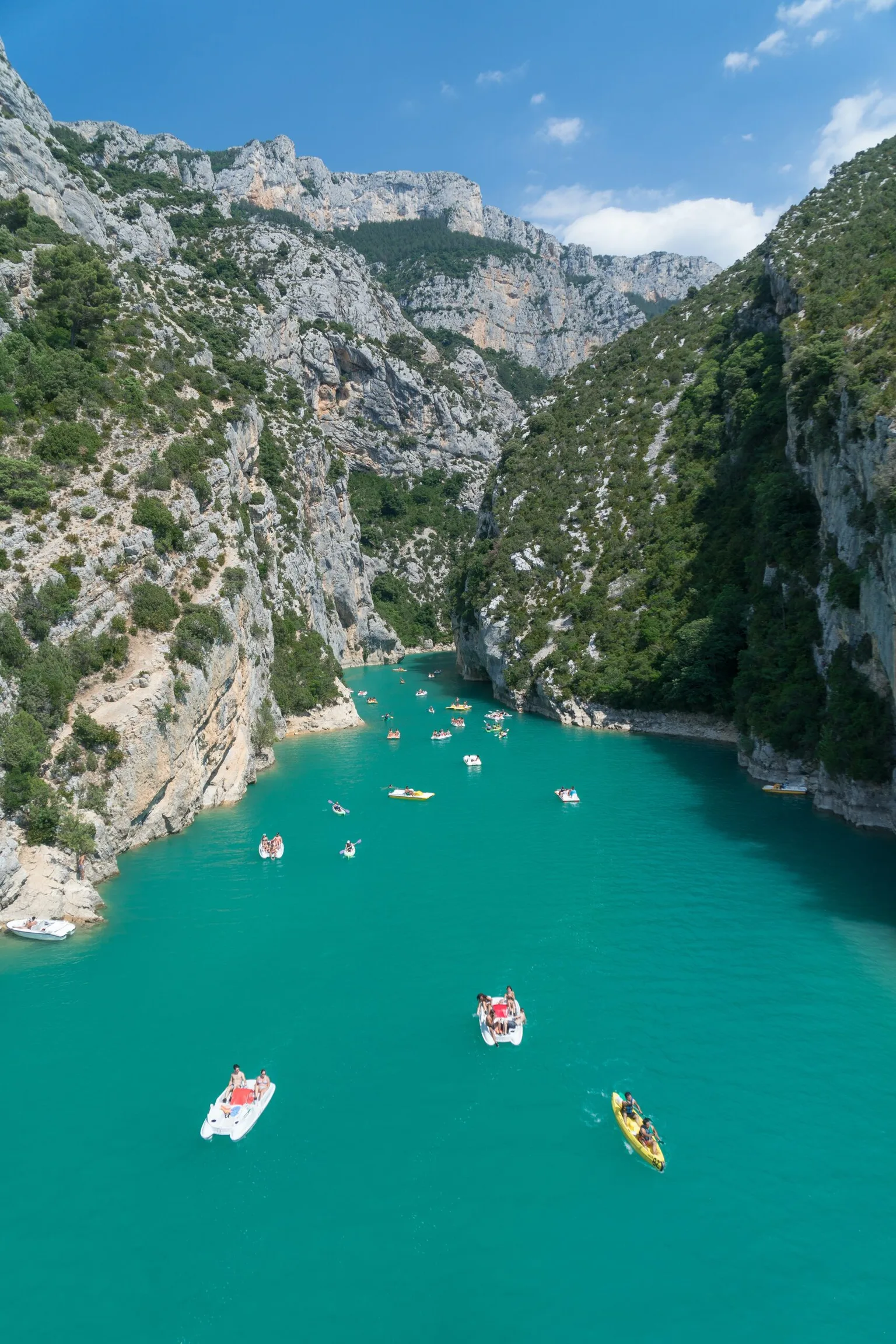 Turquoise river winding through steep limestone gorges with small boats and kayaks drifting beneath sunlit cliffs.