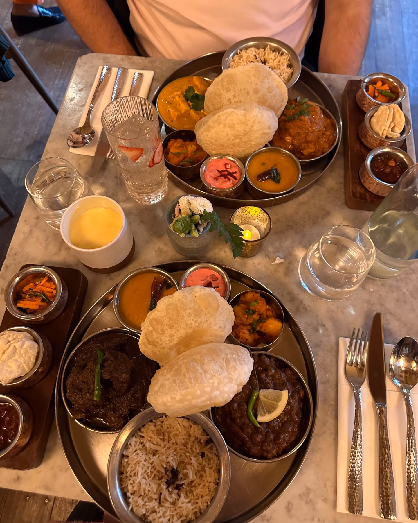 Two elaborate Indian meal platters with curries, rice and papadums are served on a marble table with drinks