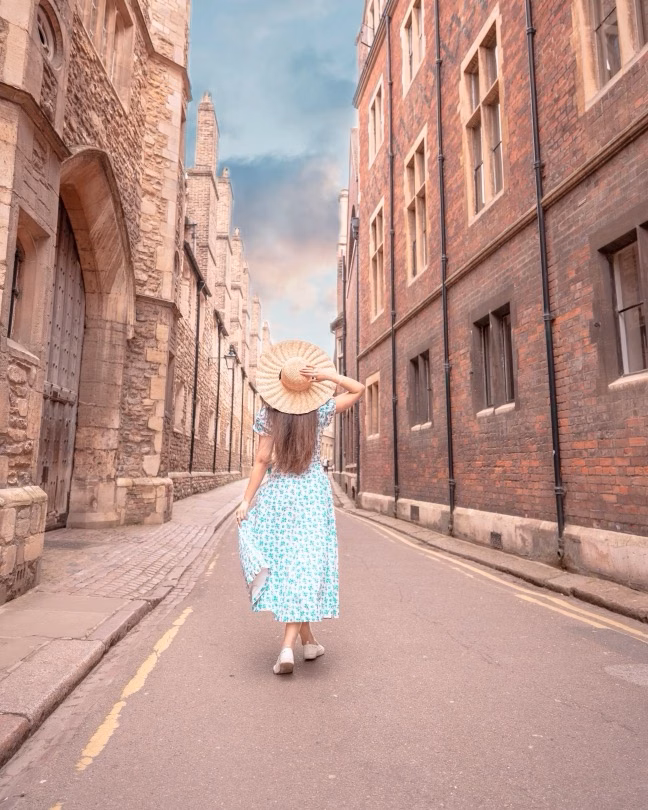 Woman in a sunhat and floral dress walking down a quiet historic street between old buildings