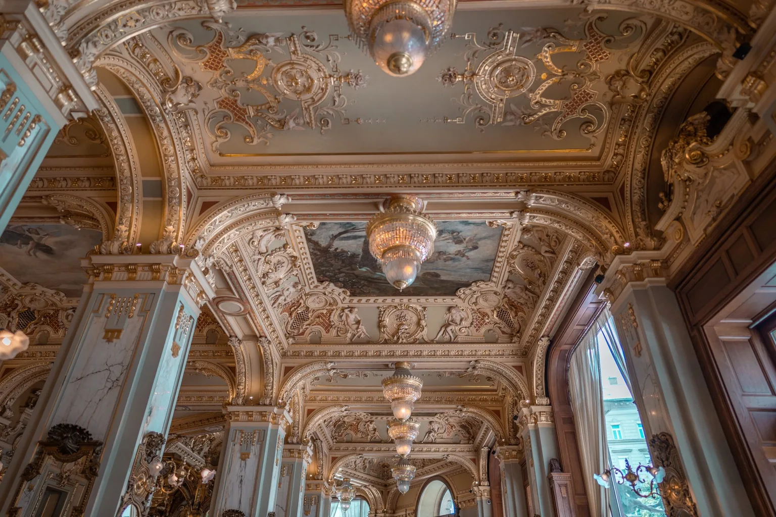 Ornate gilded Baroque ceiling with painted panels and crystal chandeliers in an opulent historic salon.