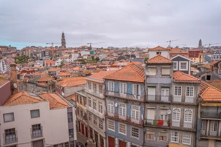 Rooftop view over a densely packed Portuguese city with terracotta tiles, ornate azulejo‑tiled façades and a distant church tower.