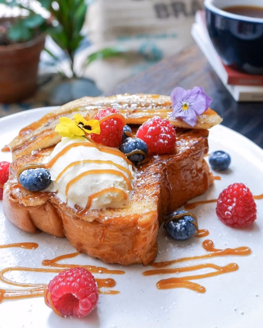 Thick French toast topped with berries, ice cream and caramel drizzle on a white plate