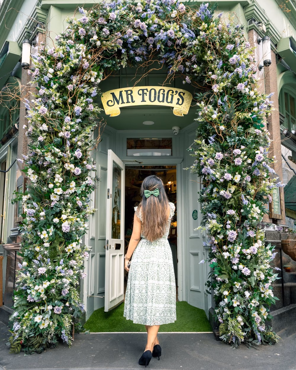 A woman in a white dress enters Mr Fogg’s through a lush floral arch