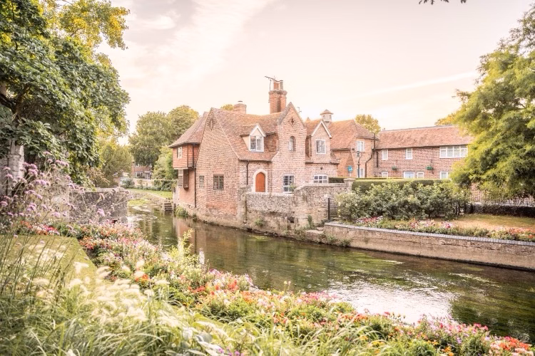 Charming brick cottages beside a calm canal, framed by lush gardens and trees