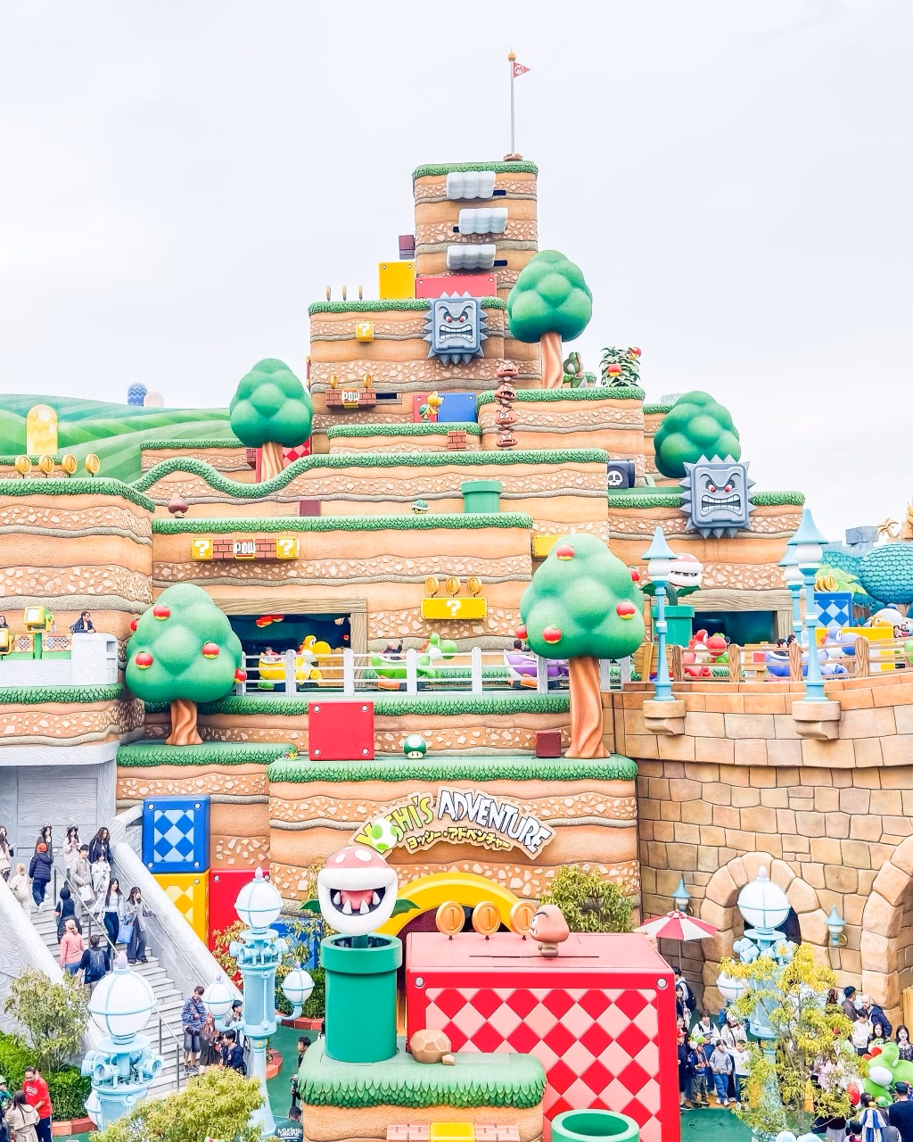 Colourful Super Nintendo World-style themed hillside with Mario game characters and visitors on stairs