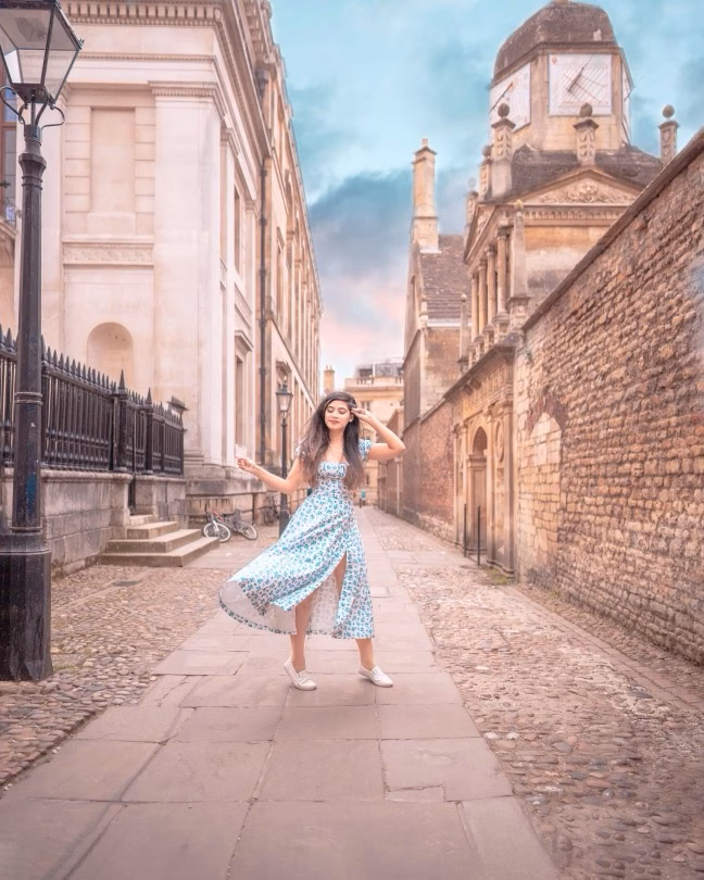 Woman in a blue dress standing on a cobbled street between historic buildings at dusk