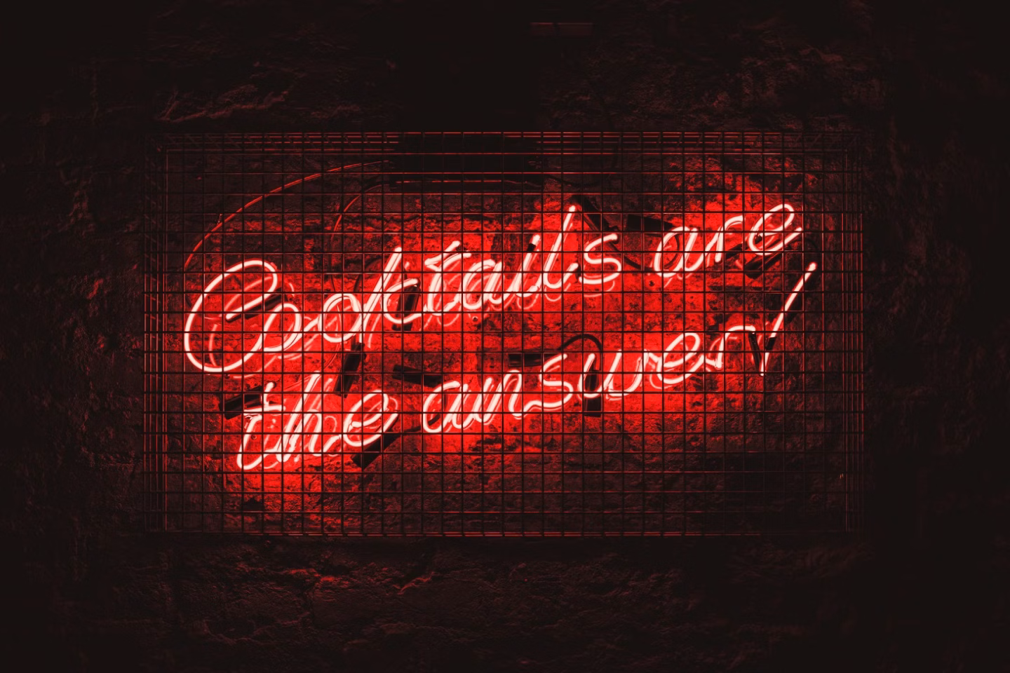 Red neon sign behind a wire mesh reading Cocktails are the answer