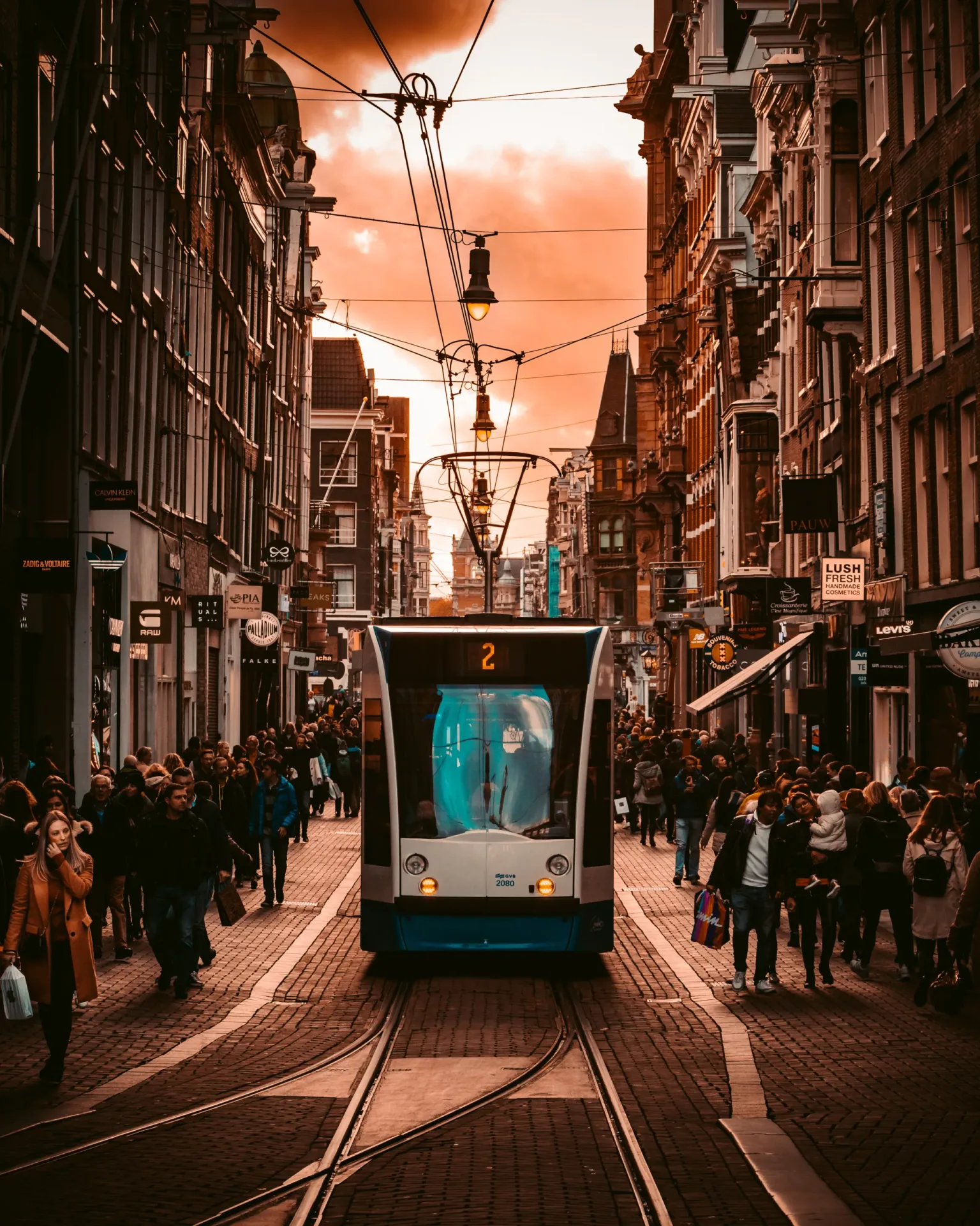 Tram number 2 traveling down a busy European shopping street at sunset, flanked by crowds and historic buildings.