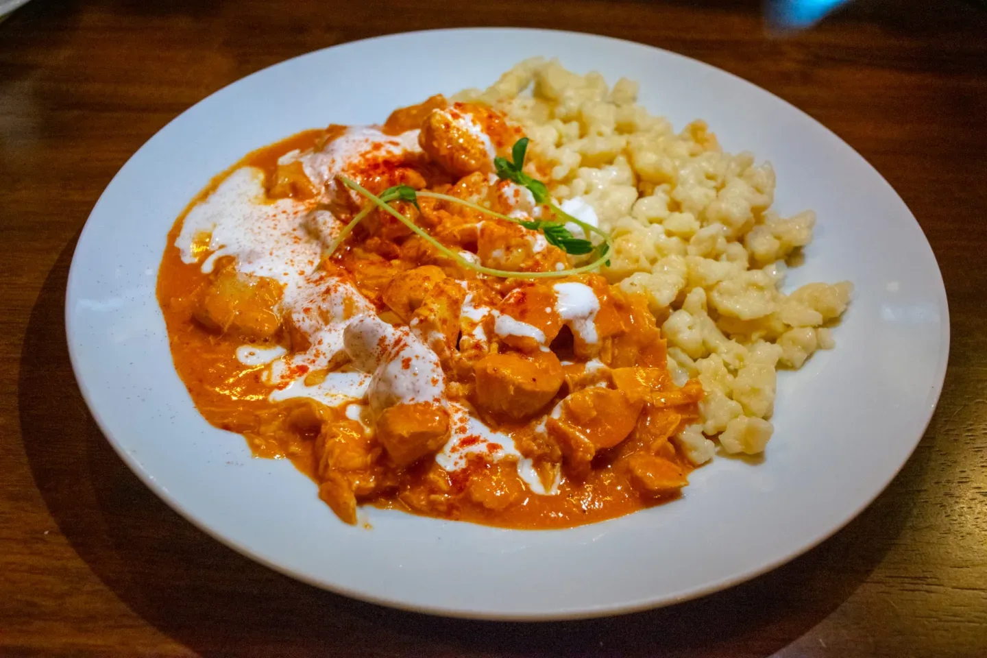Best Things to do in Budapest -Creamy paprika chicken stew served with a mound of buttery spaetzle on a white plate.