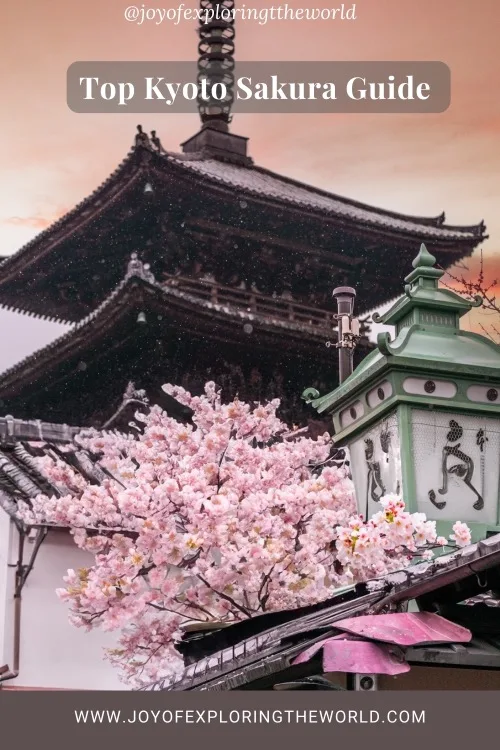 Pagoda framed by pink cherry blossoms and a decorative green lantern under a soft, peach sky in Kyoto.