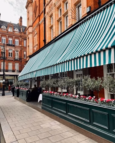 A classic red-brick building with green-and-white striped awnings lines a quiet paved street with flower boxes