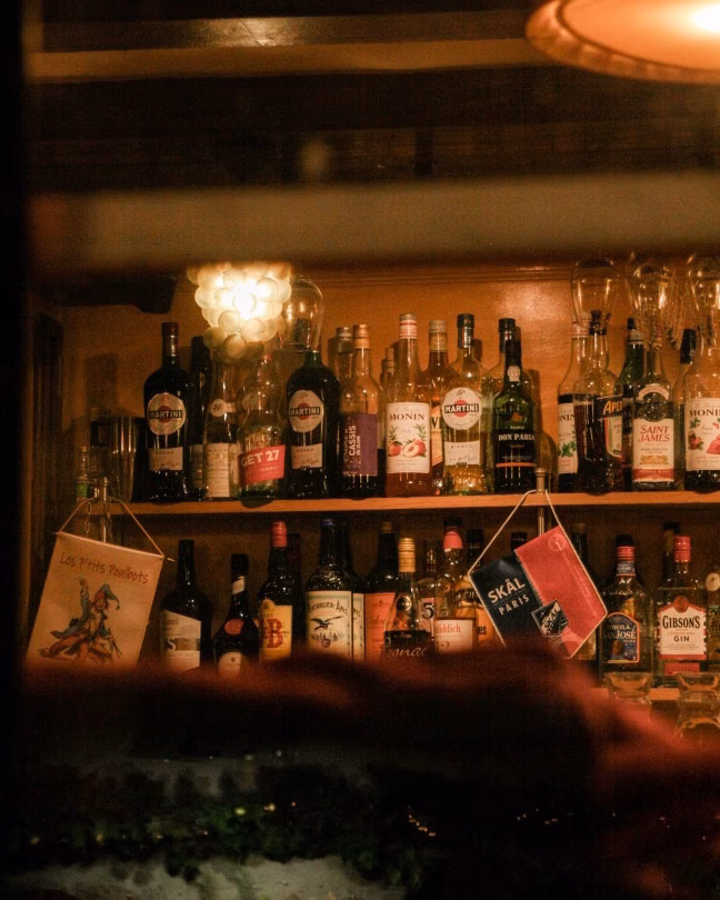 Warmly lit bar shelves lined with assorted liquor bottles and hanging labels