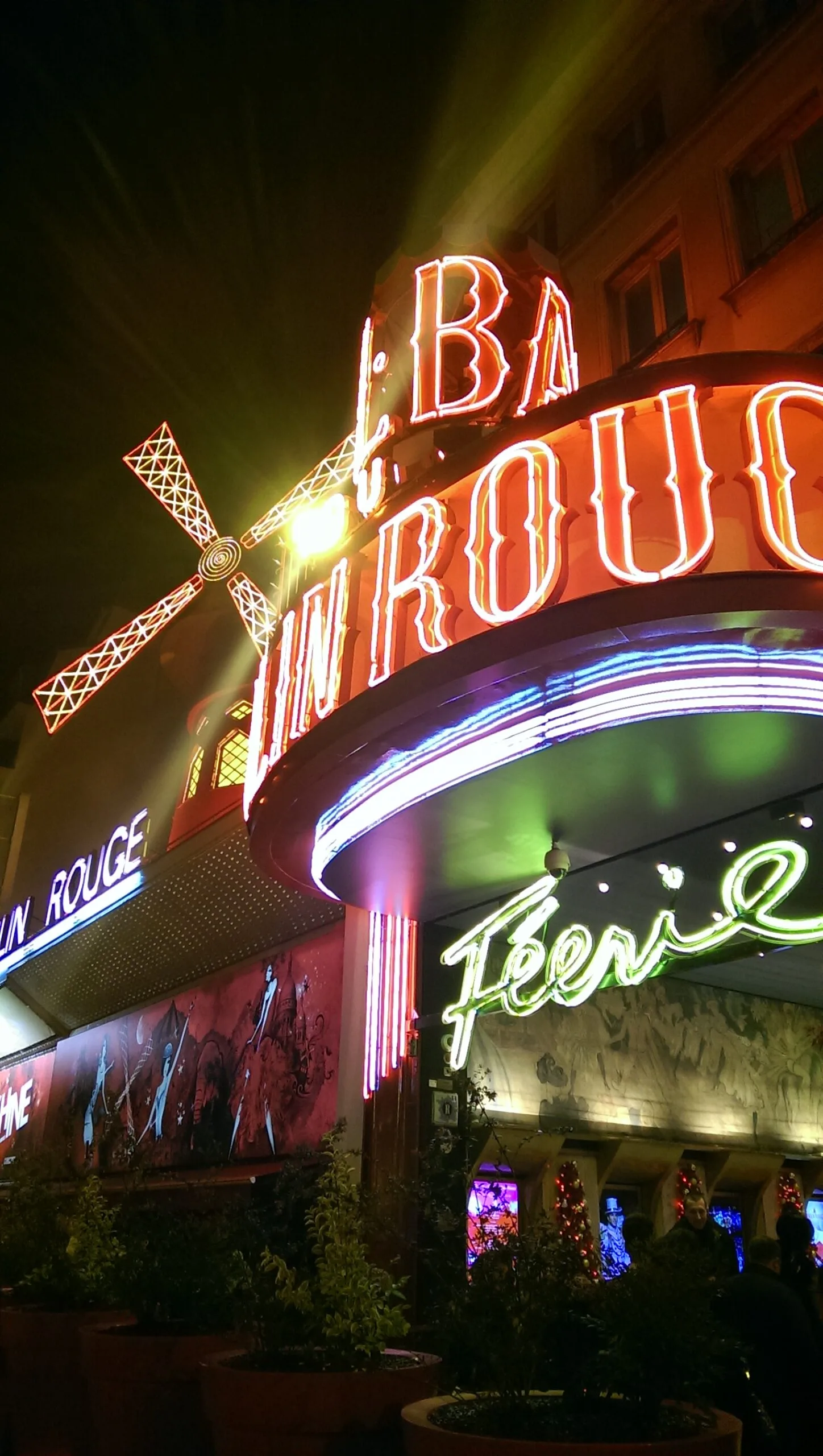Bright red neon Moulin Rouge sign and illuminated windmill above the theatre entrance at night.