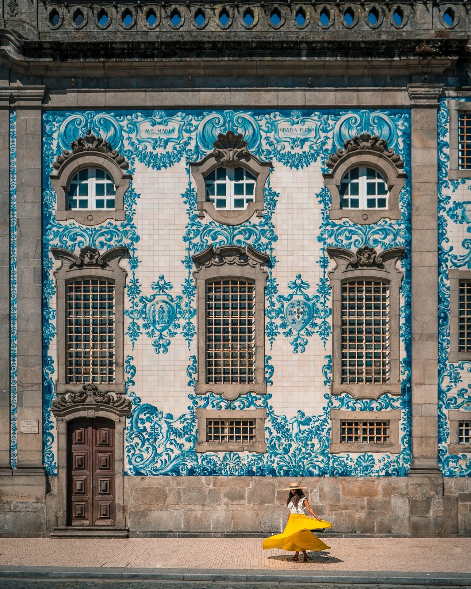 Woman in a flowing yellow skirt twirling in front of a blue-and-white azulejo-tiled baroque façade with ornate stone windows and wooden door.