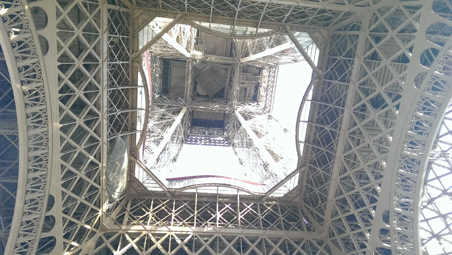 View looking straight up through the iron latticework and arches of a tall, ornate steel tower's base.