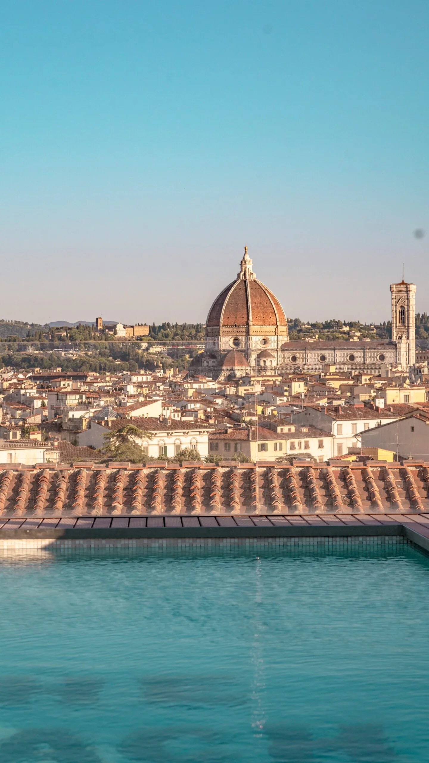 Rooftop pool in the foreground with Florence's red-tiled skyline and the Duomo's dome rising prominently against a clear blue sky.