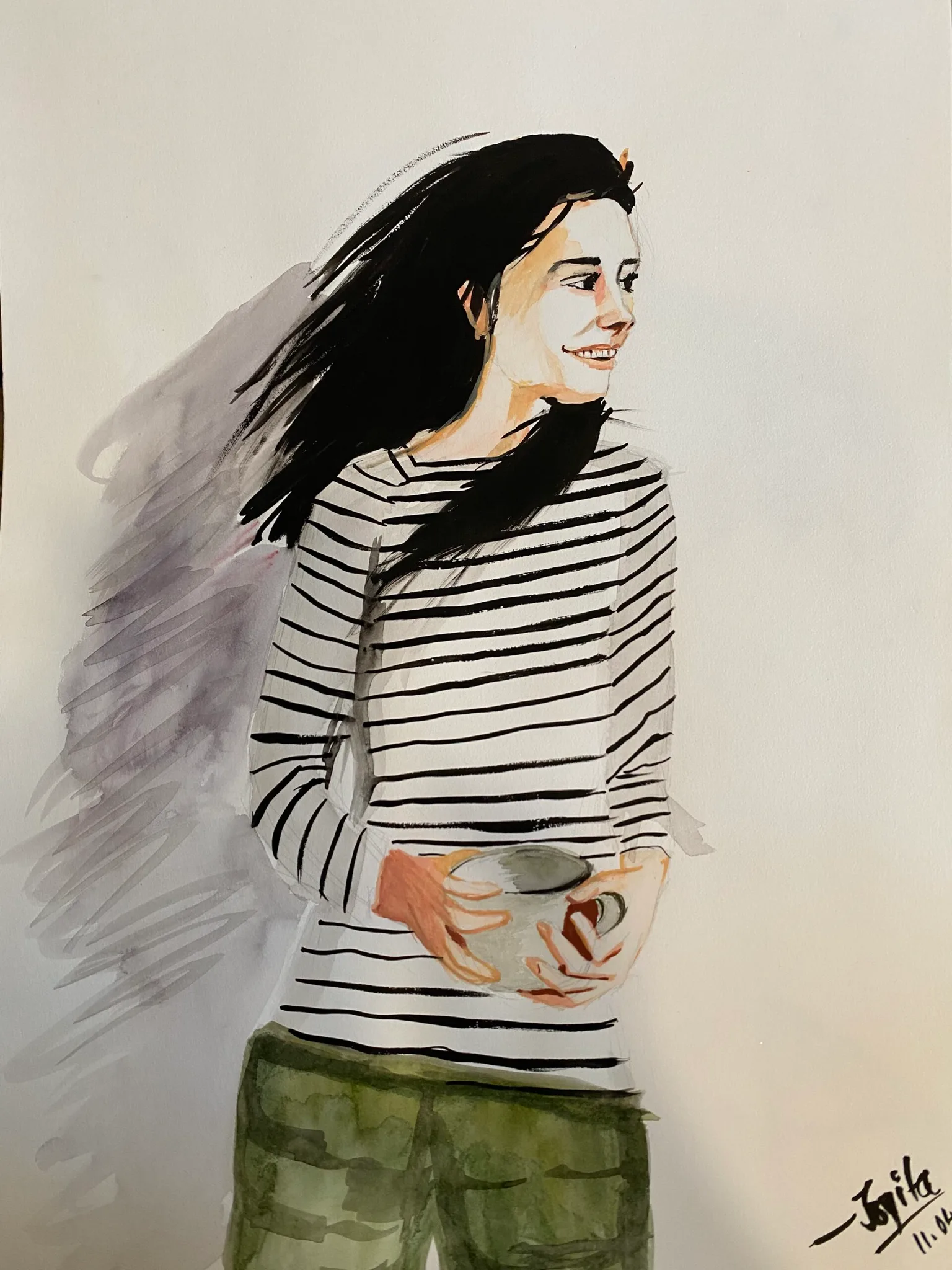 Woman in a striped top and green trousers holding a mug and smiling as her dark hair blows back in the wind.