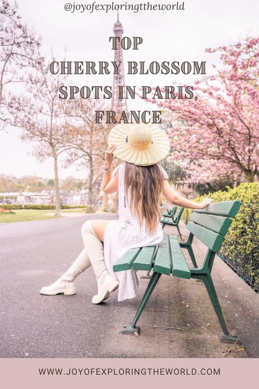 Woman in a straw hat and white dress sitting on a green bench facing cherry blossoms with the Eiffel Tower in the background.