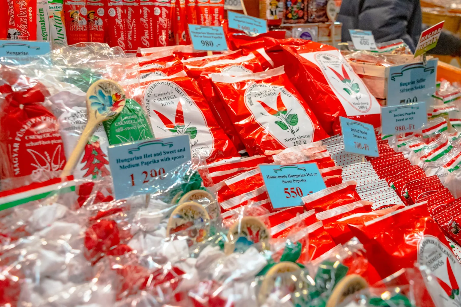 Rows of red-packaged Hungarian paprika and spice sachets with blue price tags displayed at a market stall.
