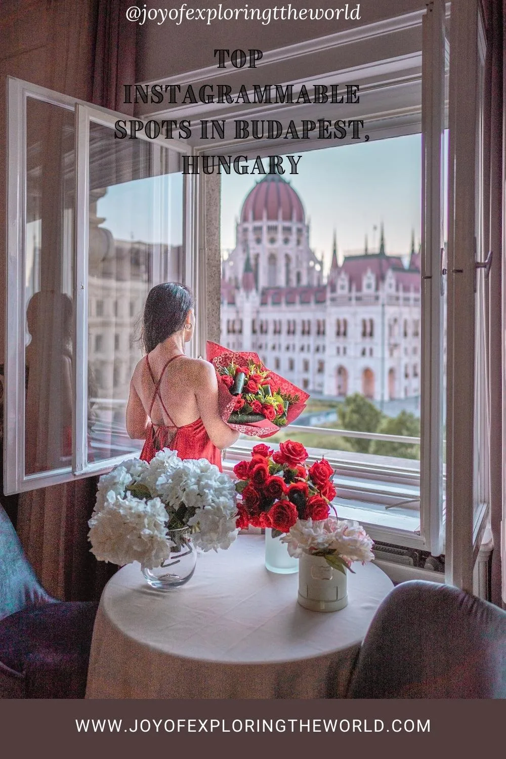 Woman in a red dress holding a bouquet at an open window overlooking the Hungarian Parliament building with vases of roses on a table.
