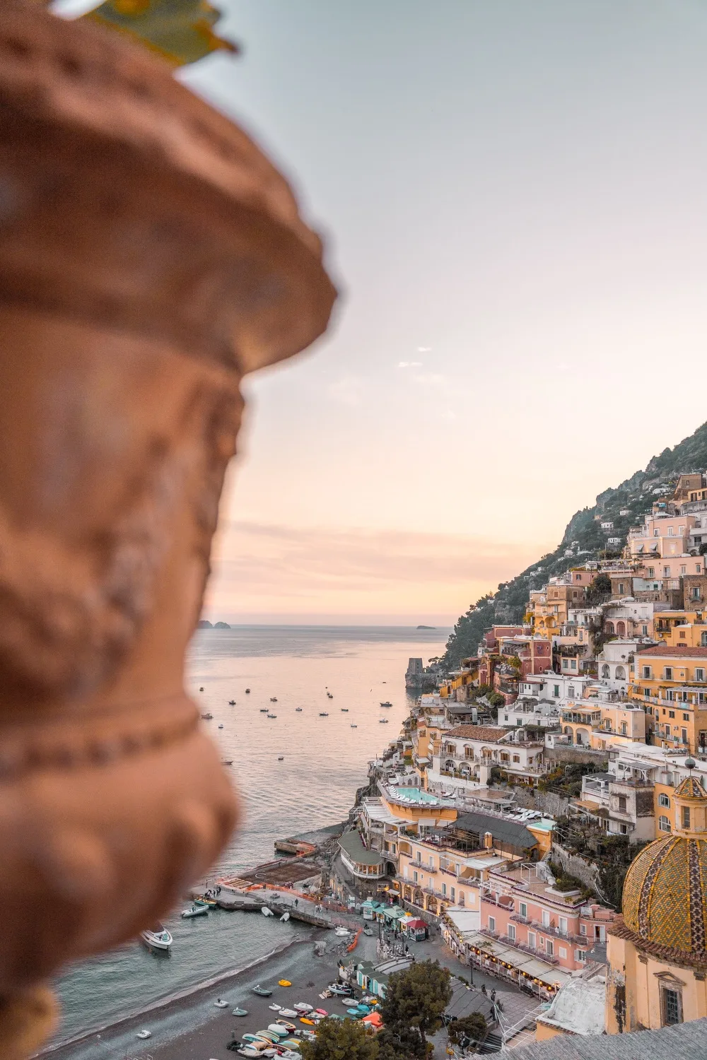 Sunset view of colourful cliffside houses and a small harbour on the Amalfi Coast with boats dotting the calm sea.