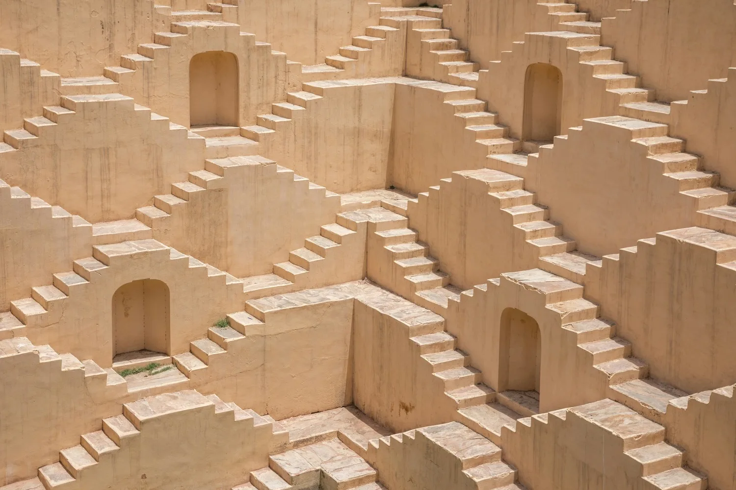 Geometric view of a pale sandstone stepwell with repeating staggered staircases and arched niches.