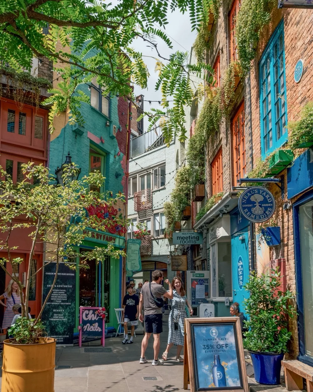 Colourful Neal’s Yard in Covent Garden ; Narrow colourful London courtyard with ivy-clad buildings, boutique shops and people strolling under dappled sunlight.