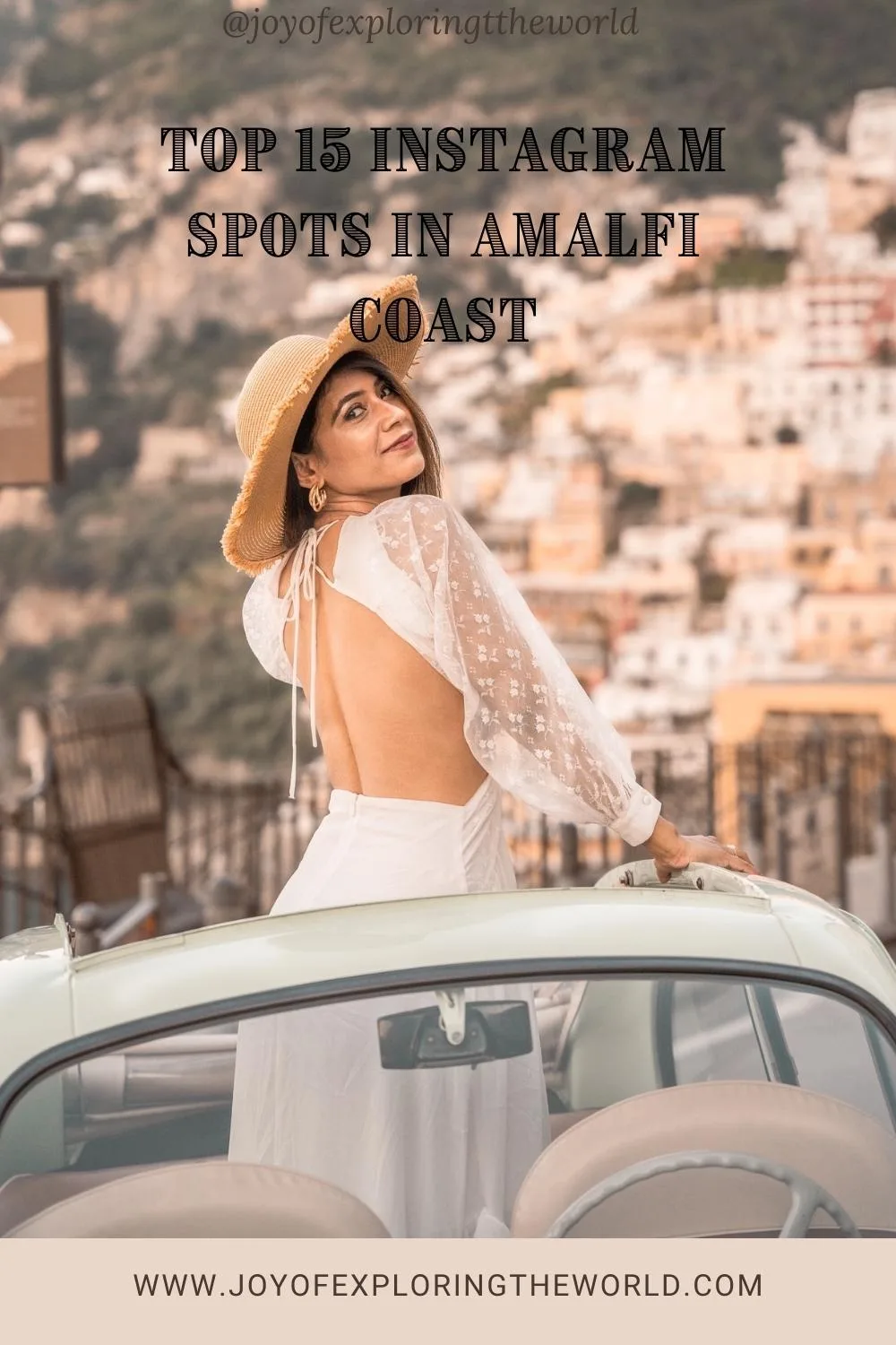Woman in a backless white dress and straw hat leaning on a vintage convertible with colourful Amalfi Coast townhouses blurred behind her.