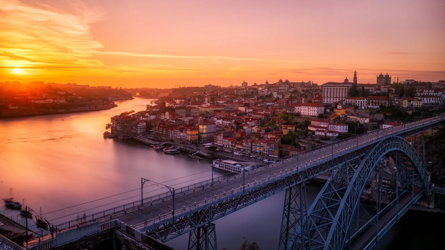 Golden sunset over Porto with the Dom Luís I double-deck iron bridge spanning the Douro River and terracotta-roofed riverside buildings.