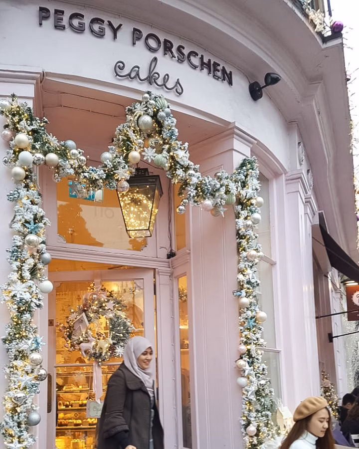 Festive Peggy Porschen Cakes shopfront decorated with Christmas garlands and lights, with shoppers passing by