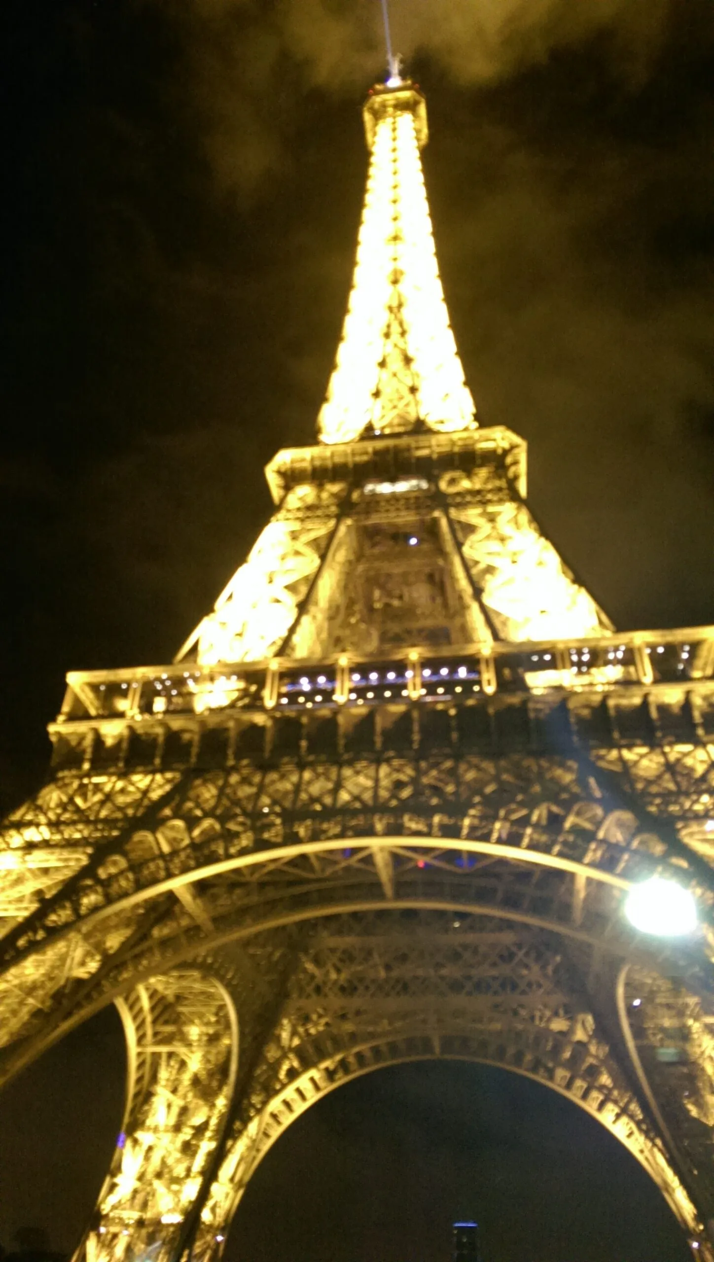 Nighttime view looking up at the illuminated Eiffel Tower's golden iron arches and latticework against a dark sky