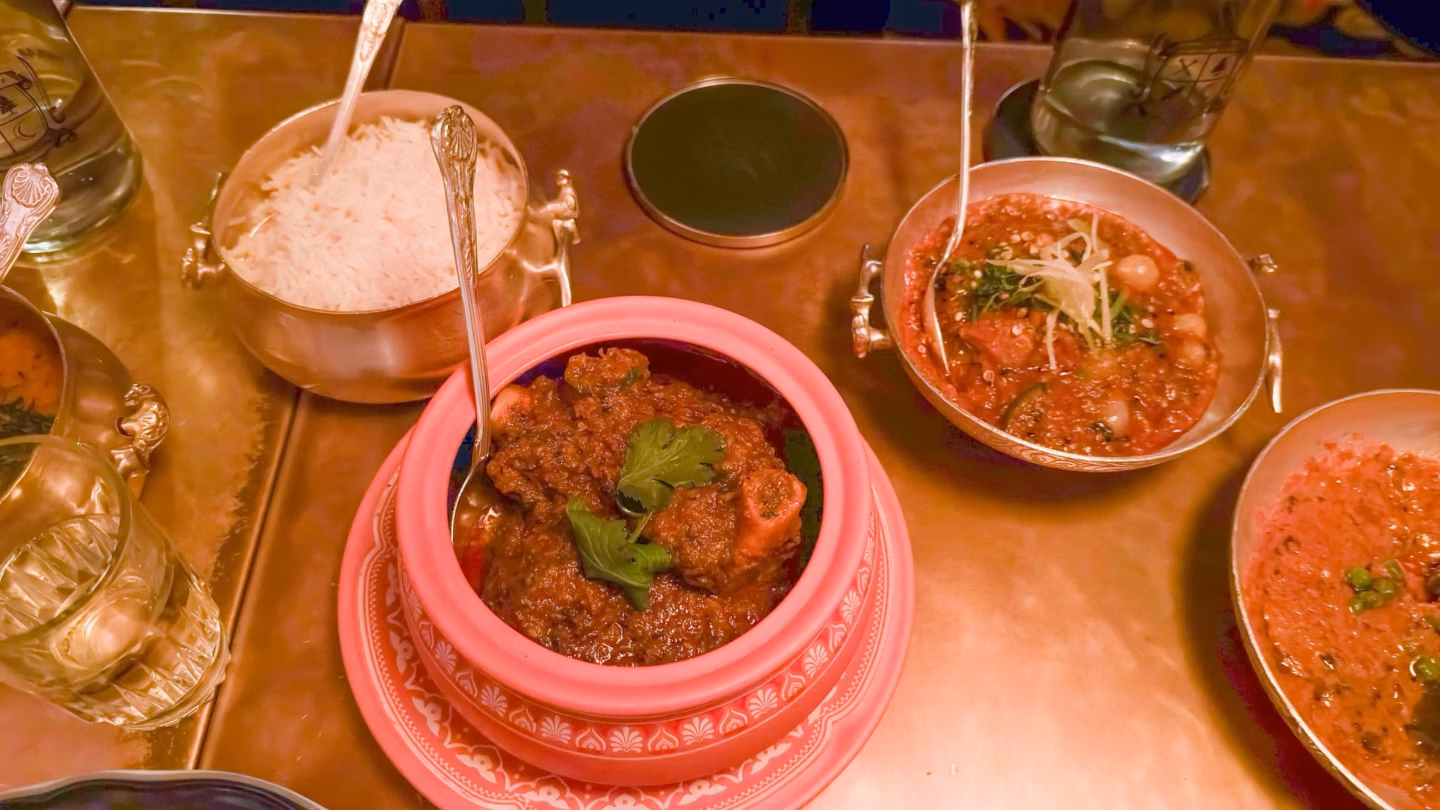 A spread of Indian dishes served in ornate bowls on a copper table, including rice and rich curries