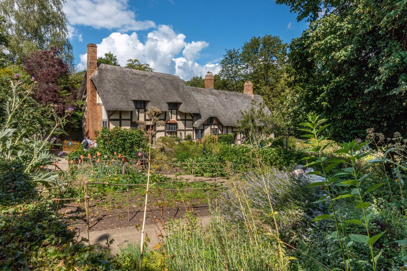 Thatched cottage surrounded by a lush garden under a blue sky