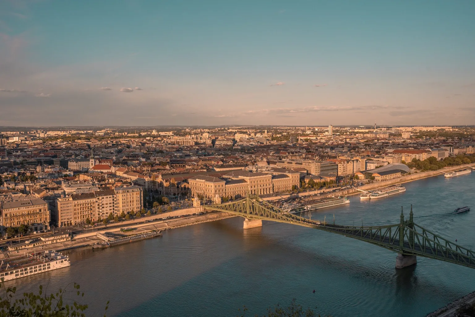 Sunlit panoramic view of Budapest with the green Liberty Bridge crossing the Danube and historic riverside buildings.